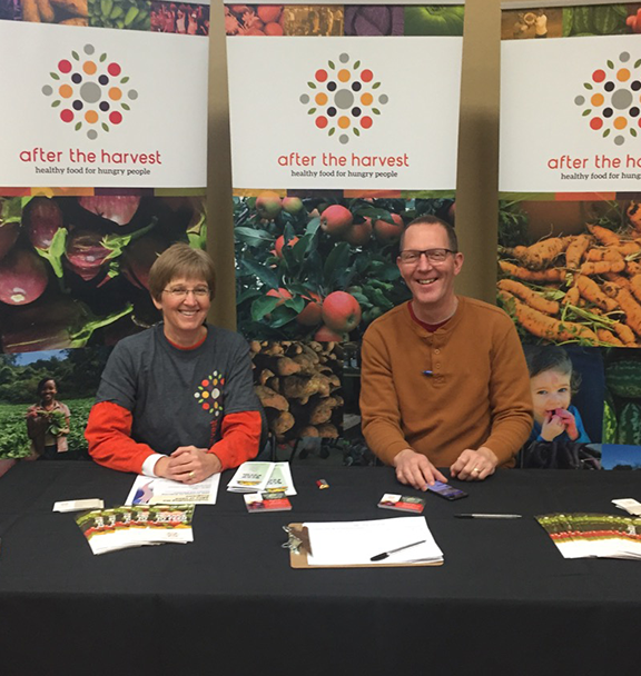 A man and woman who are yambassadors are sitting in an After the Harvest booth
